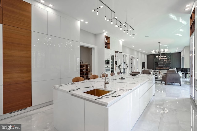 kitchen featuring white cabinetry, sink, hanging light fixtures, and a large island with sink