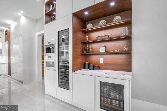 bar with oven, white cabinets, light stone counters, and beverage cooler