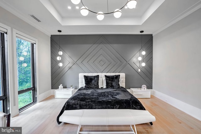 bedroom featuring light hardwood / wood-style flooring, ornamental molding, and a tray ceiling