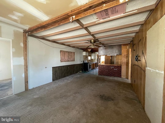 basement featuring dark carpet, wooden walls, and ceiling fan