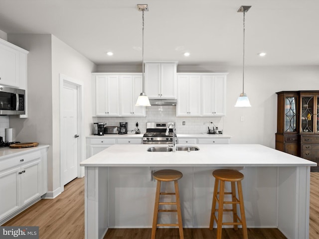 kitchen featuring appliances with stainless steel finishes, decorative light fixtures, white cabinetry, and an island with sink