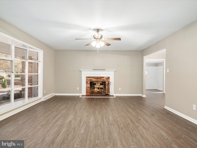 unfurnished living room featuring a brick fireplace, dark hardwood / wood-style floors, and ceiling fan