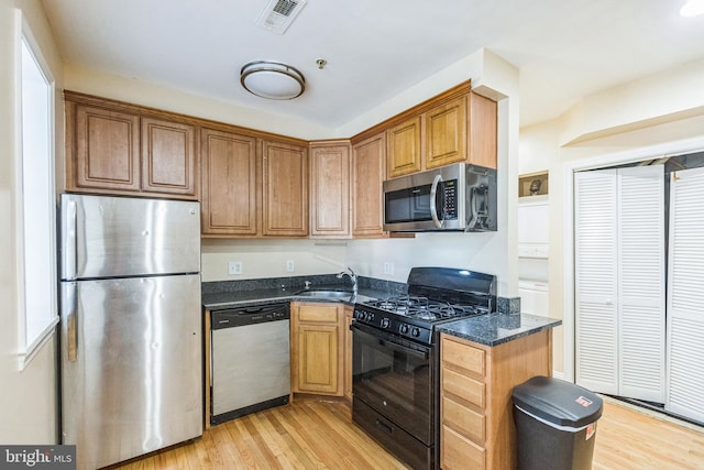 kitchen featuring light hardwood / wood-style floors, dark stone countertops, stacked washer / dryer, sink, and stainless steel appliances