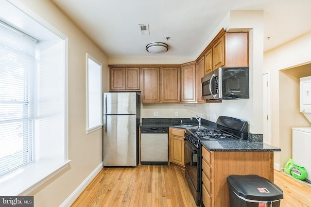 kitchen with stainless steel appliances, plenty of natural light, dark stone countertops, and light wood-type flooring