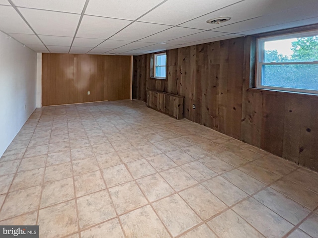 basement featuring wooden walls and a paneled ceiling