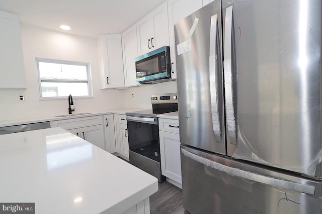 kitchen with stainless steel appliances, a sink, white cabinets, light countertops, and dark wood-style floors