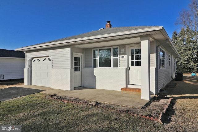 exterior space with brick siding, a chimney, central AC unit, a garage, and driveway