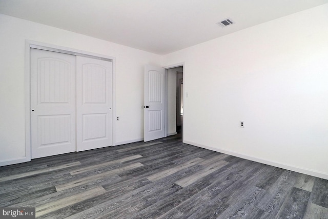 unfurnished bedroom featuring dark wood-type flooring, a closet, visible vents, and baseboards