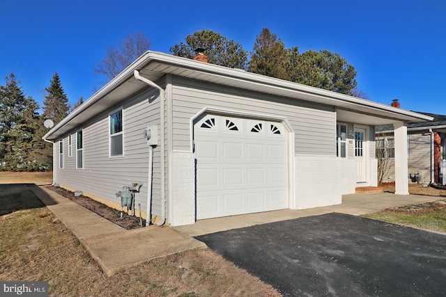 view of side of home featuring a garage, a chimney, and aphalt driveway