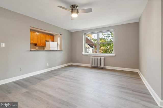 empty room with radiator heating unit, light wood-type flooring, and ceiling fan