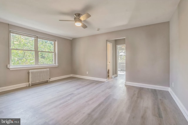 spare room with ceiling fan, radiator, light wood-type flooring, and a wealth of natural light