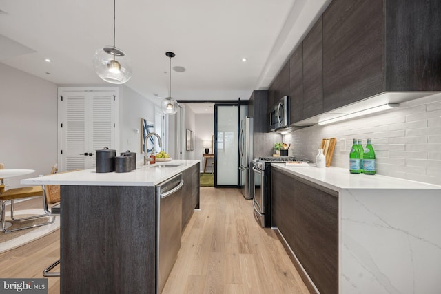 kitchen with appliances with stainless steel finishes, a barn door, light hardwood / wood-style flooring, sink, and decorative light fixtures