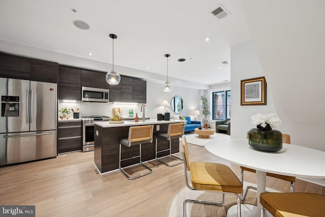 kitchen featuring appliances with stainless steel finishes, dark brown cabinets, hanging light fixtures, light hardwood / wood-style floors, and a breakfast bar area