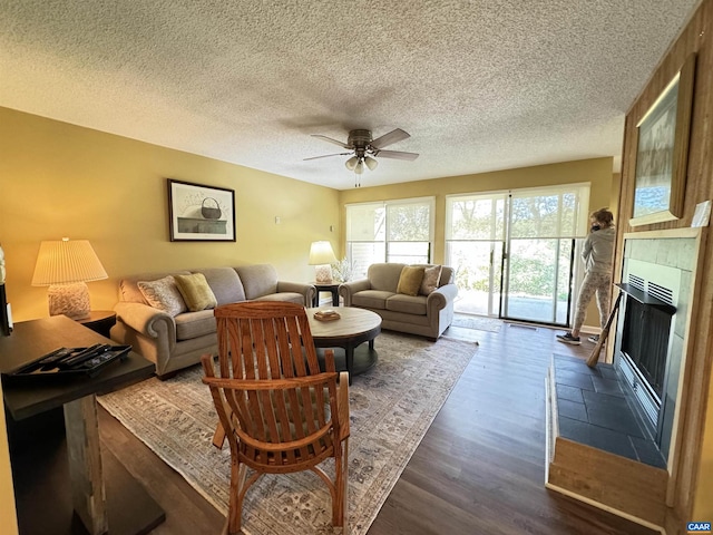 living room with ceiling fan, dark wood-type flooring, a tile fireplace, and a textured ceiling