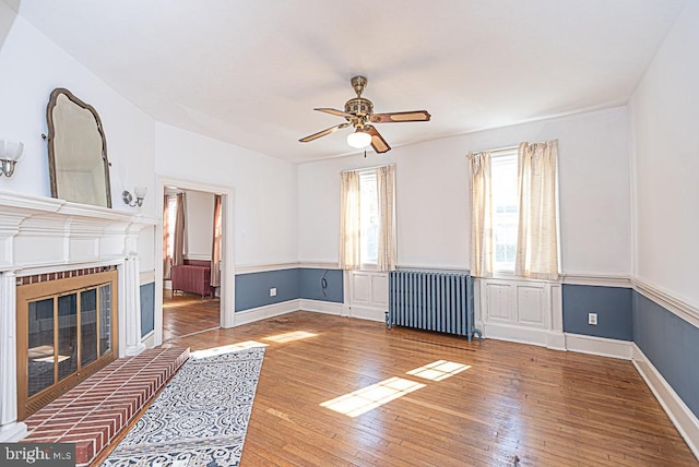 unfurnished living room with ceiling fan, a brick fireplace, hardwood / wood-style flooring, and radiator