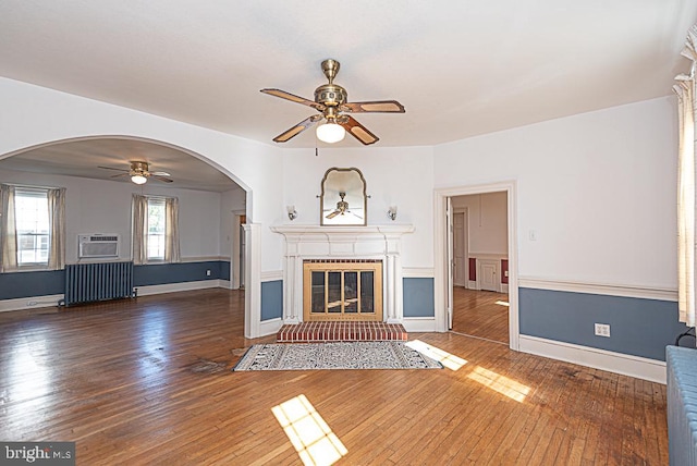 unfurnished living room with a wall mounted air conditioner, ceiling fan, radiator heating unit, and dark hardwood / wood-style flooring