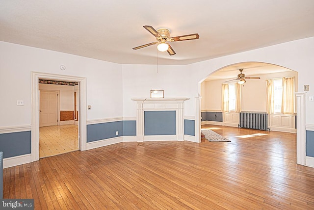 unfurnished living room with ceiling fan, light wood-type flooring, and radiator