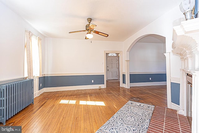 unfurnished living room with dark wood-type flooring, ceiling fan, and radiator