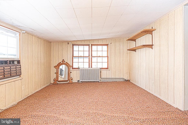 carpeted empty room featuring lofted ceiling, wooden walls, and radiator