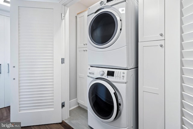 laundry area featuring cabinets, dark wood-type flooring, and stacked washing maching and dryer