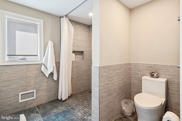 bathroom featuring a shower with shower curtain, toilet, and tile walls