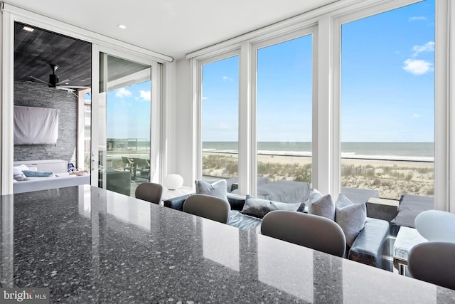 dining room with a view of the beach, expansive windows, a water view, and ceiling fan