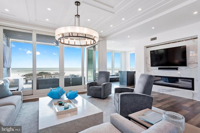 living room with a high end fireplace, plenty of natural light, a water view, and hardwood / wood-style floors