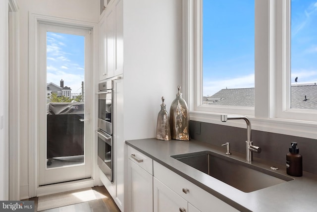 kitchen featuring white cabinets, hardwood / wood-style floors, stainless steel double oven, and sink