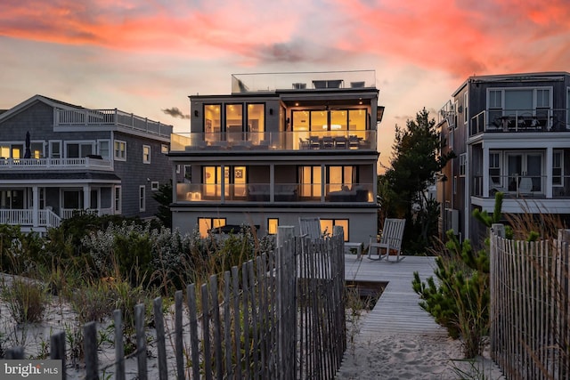 back house at dusk featuring solar panels, a balcony, and a deck