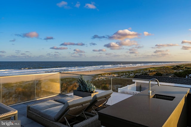 patio terrace at dusk with sink, a water view, and a view of the beach