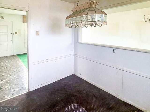 unfurnished dining area featuring a chandelier and carpet