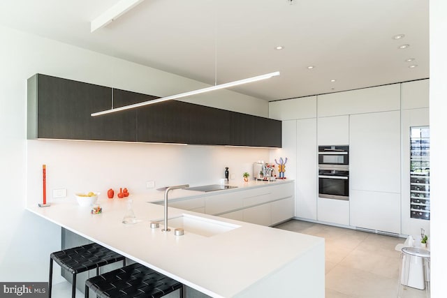 kitchen featuring a kitchen breakfast bar, sink, kitchen peninsula, double oven, and white cabinetry