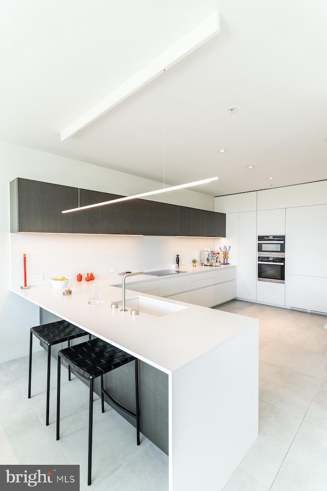 kitchen featuring a breakfast bar, stainless steel double oven, sink, kitchen peninsula, and white cabinetry