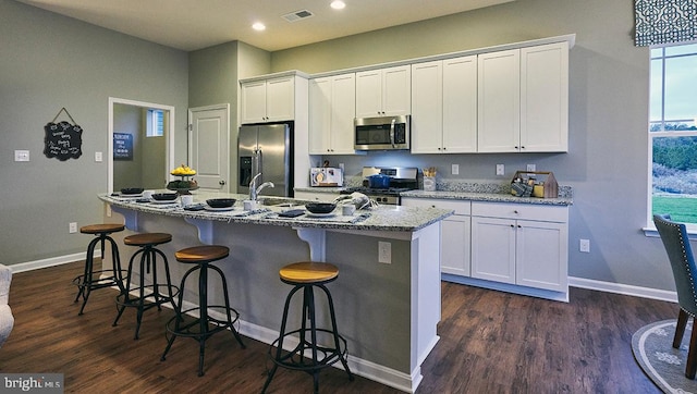 kitchen with white cabinets, a center island with sink, stainless steel appliances, and dark wood-type flooring