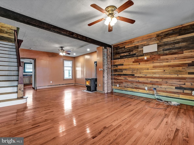 unfurnished living room with beamed ceiling, a wood stove, light hardwood / wood-style flooring, a baseboard radiator, and a textured ceiling