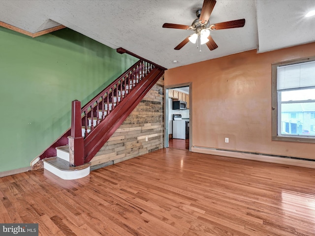 unfurnished living room with ceiling fan, baseboard heating, light hardwood / wood-style flooring, and a textured ceiling