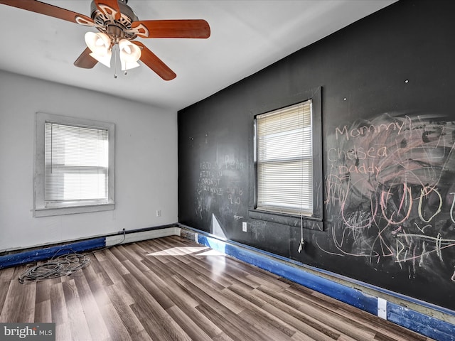 empty room featuring plenty of natural light, a baseboard heating unit, wood-type flooring, and ceiling fan