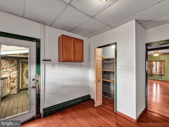 interior space featuring ceiling fan, a paneled ceiling, hardwood / wood-style floors, and a baseboard heating unit