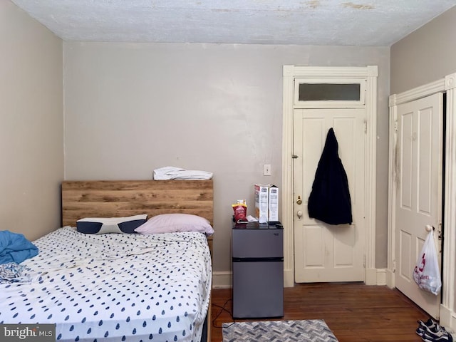 bedroom with dark wood-type flooring, a textured ceiling, and stainless steel fridge