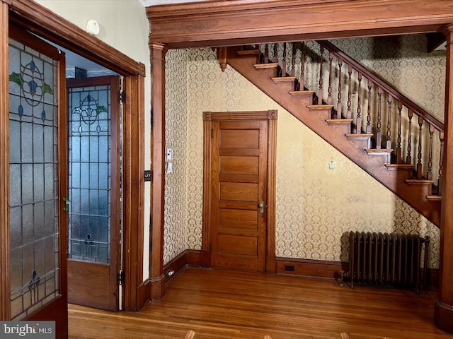 staircase featuring radiator heating unit, wood-type flooring, and ornate columns