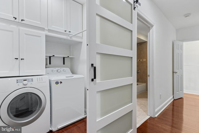 laundry room featuring cabinets, dark hardwood / wood-style floors, a barn door, and washing machine and clothes dryer