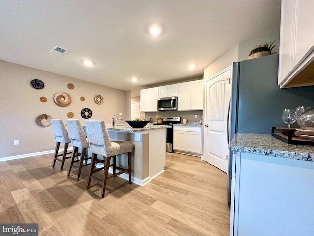 kitchen featuring stainless steel appliances, white cabinets, light stone counters, and light wood-type flooring