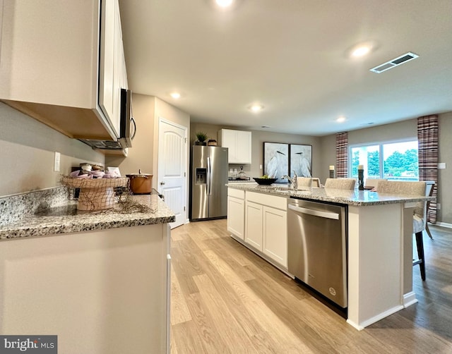 kitchen with light hardwood / wood-style flooring, light stone countertops, an island with sink, appliances with stainless steel finishes, and white cabinetry