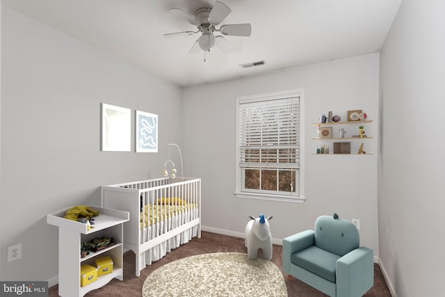 carpeted bedroom with a crib and ceiling fan