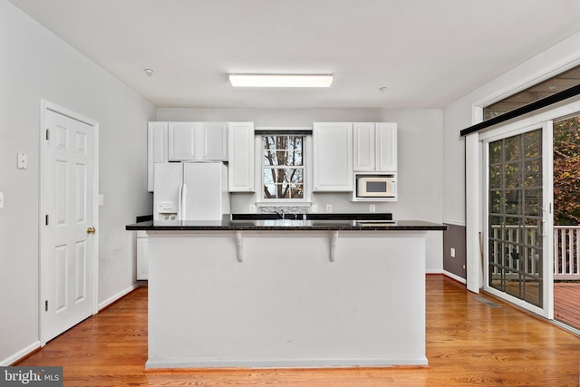 kitchen with white appliances, white cabinetry, a breakfast bar, and light hardwood / wood-style floors