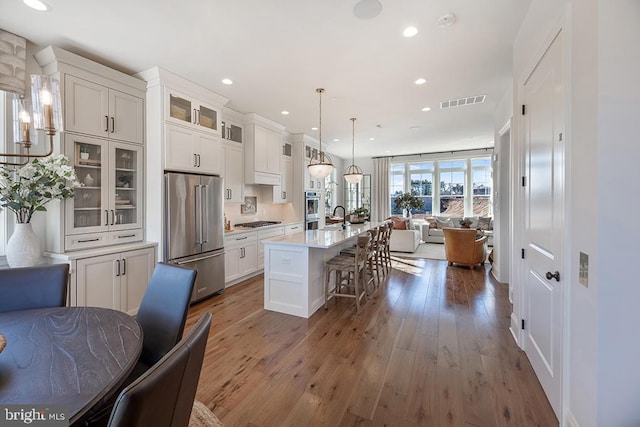 kitchen featuring hanging light fixtures, a kitchen island with sink, dark wood-type flooring, appliances with stainless steel finishes, and a kitchen breakfast bar