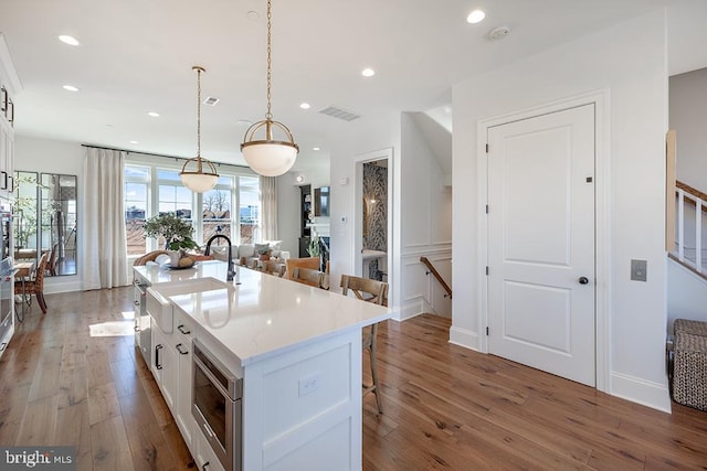 kitchen with dark hardwood / wood-style floors, a center island with sink, hanging light fixtures, a kitchen bar, and white cabinetry