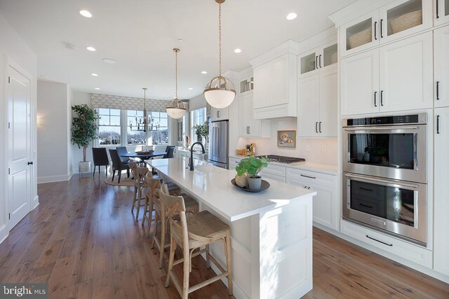 kitchen featuring an island with sink, dark hardwood / wood-style floors, stainless steel appliances, white cabinets, and a kitchen bar