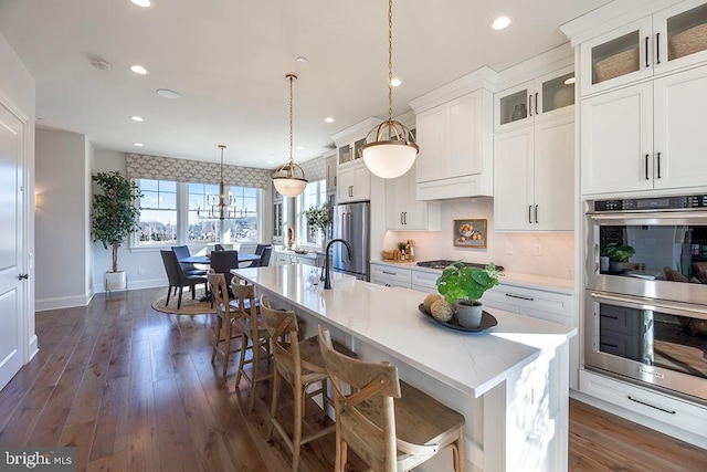 kitchen featuring a kitchen island with sink, stainless steel appliances, a kitchen bar, and white cabinetry