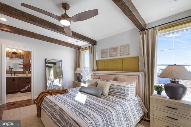 bedroom featuring light wood-type flooring, beamed ceiling, ceiling fan, and connected bathroom